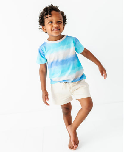 Child wearing a blue ombre shirt and ivory bamboo-cotton shorts on a white background
