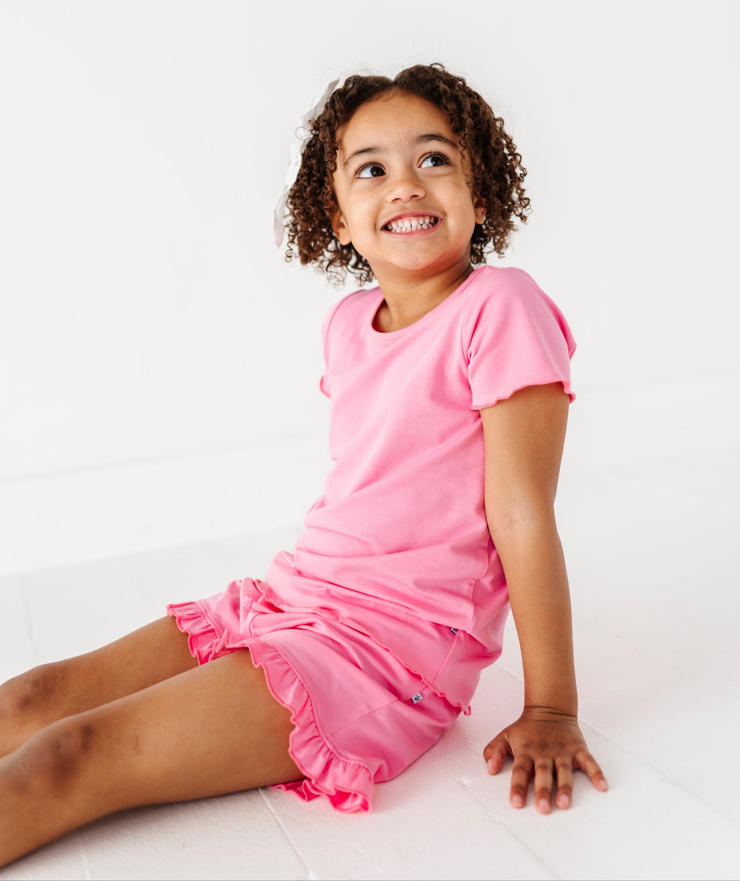 Young girl wearing a pink bamboo/cotton top and matching bamboo/cotton shorts sitting on a white background