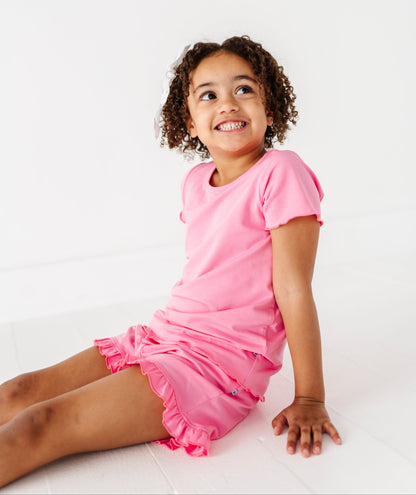 Young girl wearing a pink bamboo/cotton top and matching bamboo/cotton shorts sitting on a white background