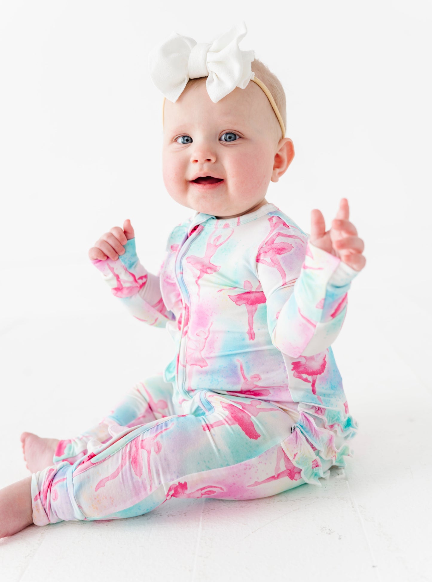 Baby wearing a colorful ballet bamboo onesie with a white bow on a white background