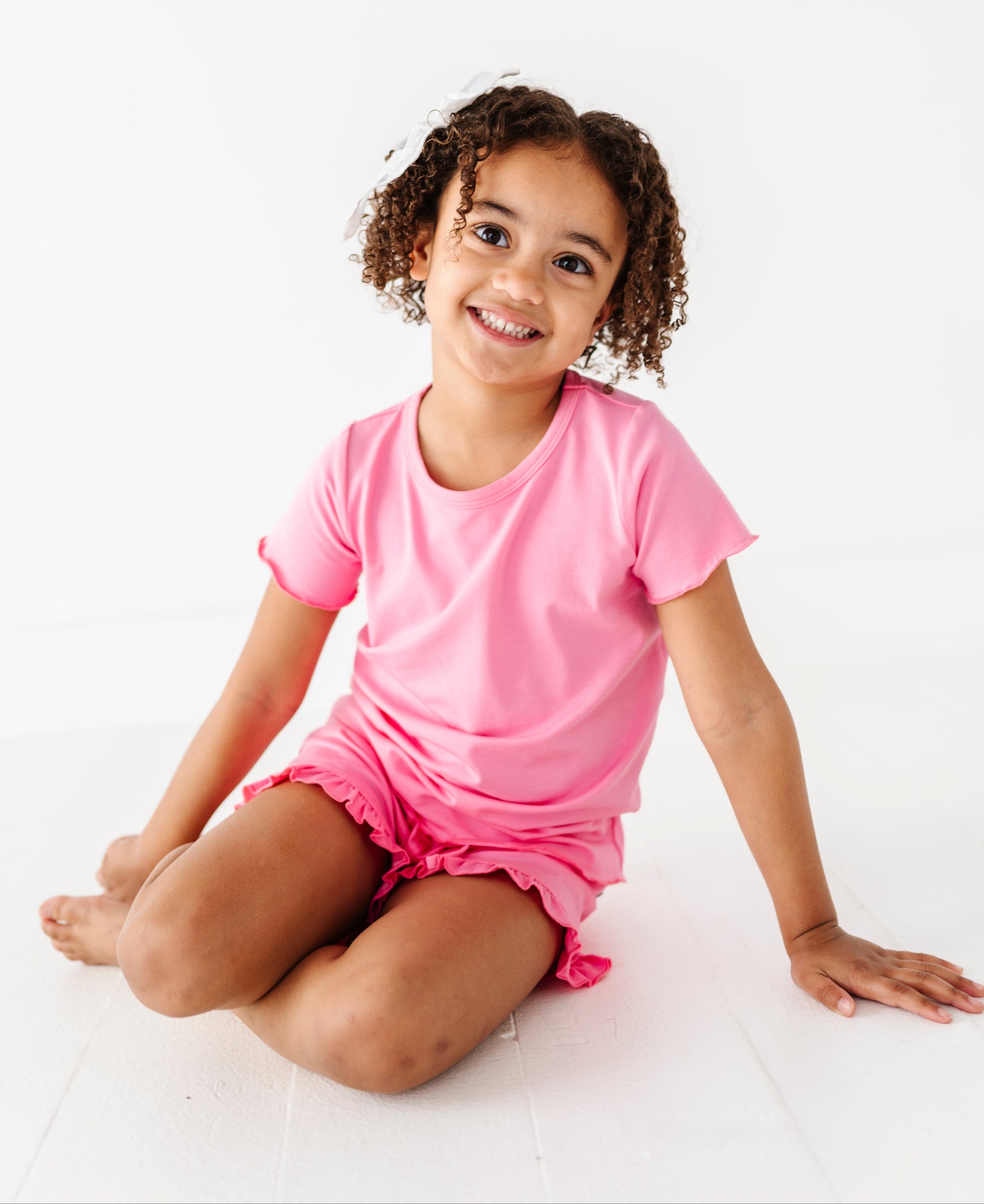 Young girl wearing a pink bamboo cotton outfit sitting on a white background