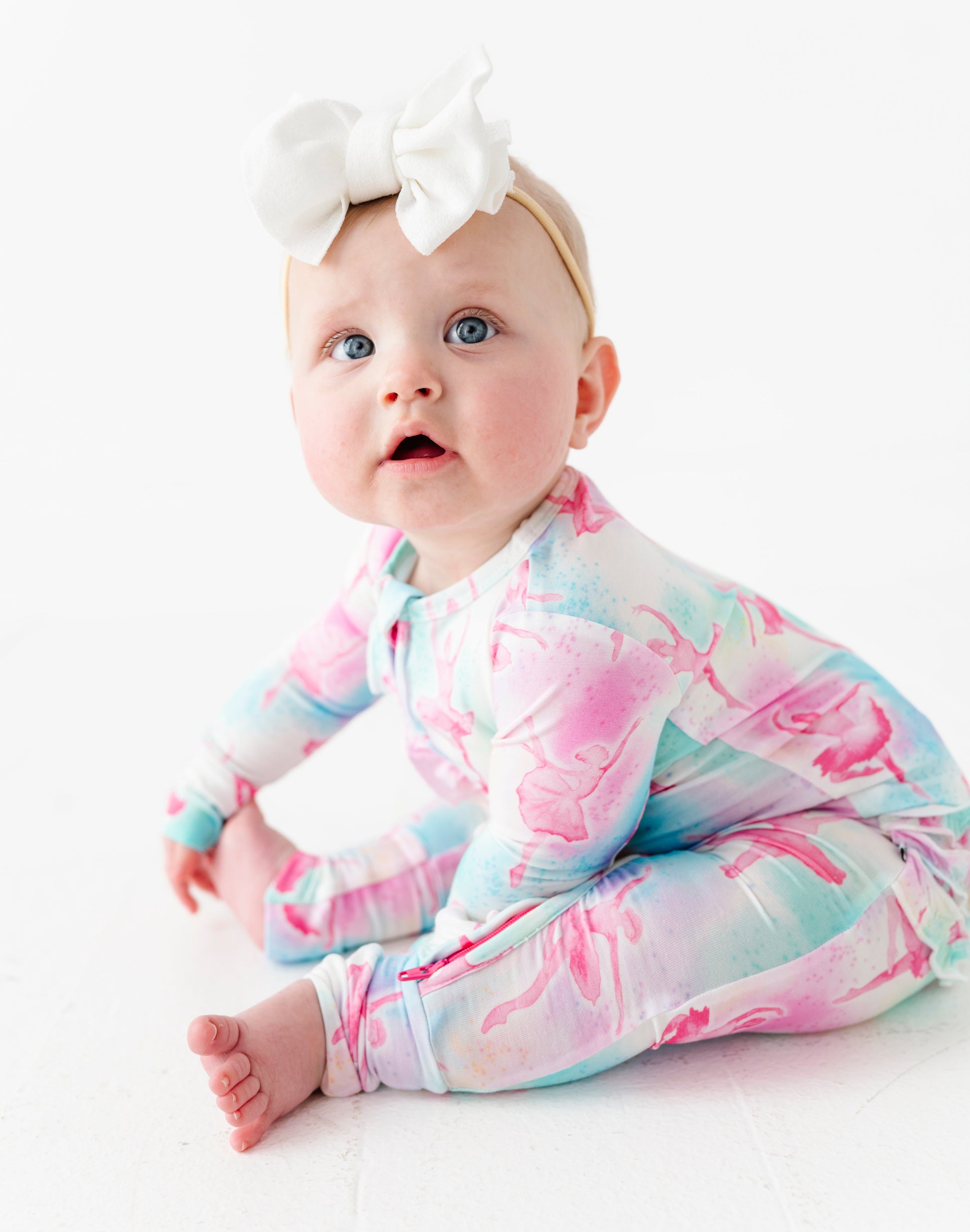 Baby wearing a colorful banbii onesie with a white bow on a light background