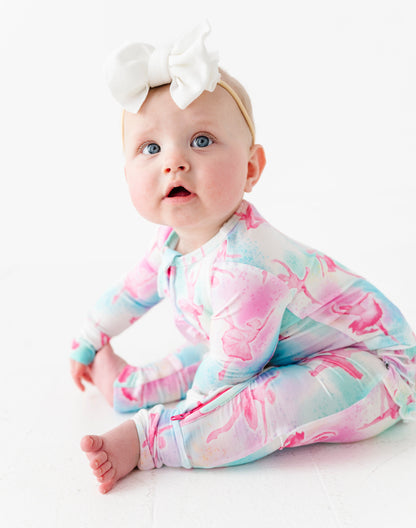 Baby wearing a colorful banbii onesie with a white bow on a light background