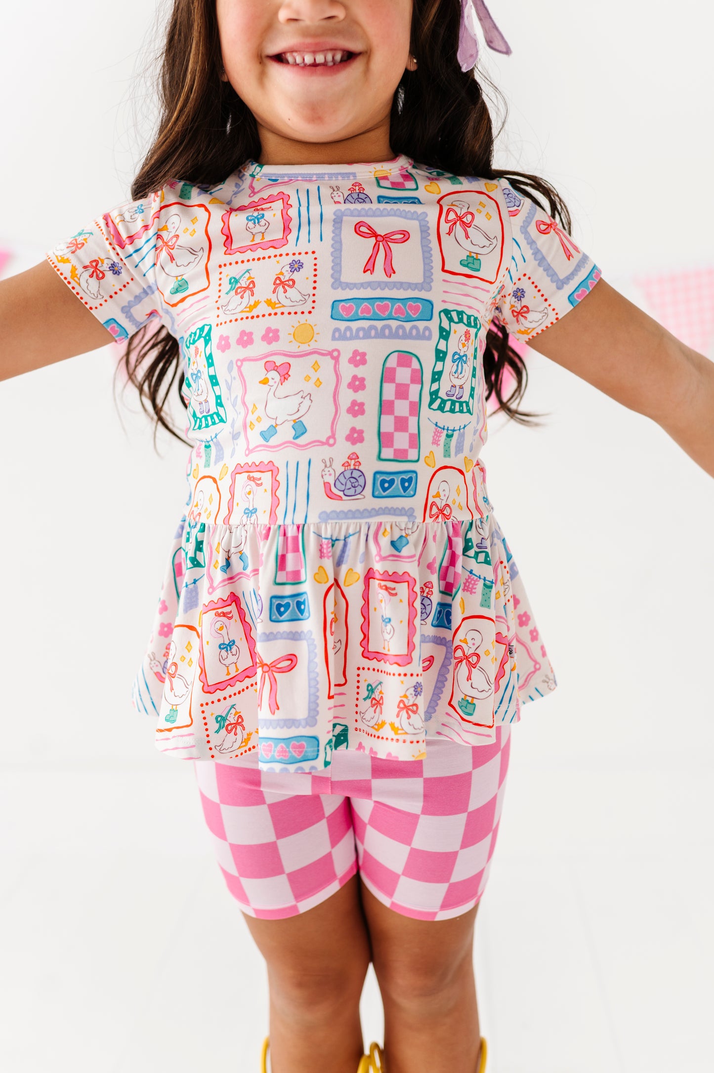 Child wearing a patterned top and pink checkered shorts on a white background