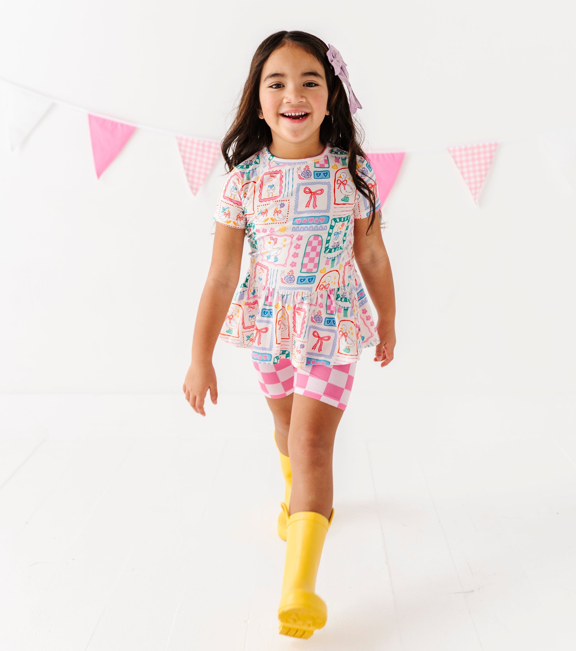 Girl in a peplum top with pink checkered shorts and yellow rain boots on a white background 