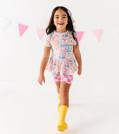 Girl in a peplum top with pink checkered shorts and yellow rain boots on a white background 