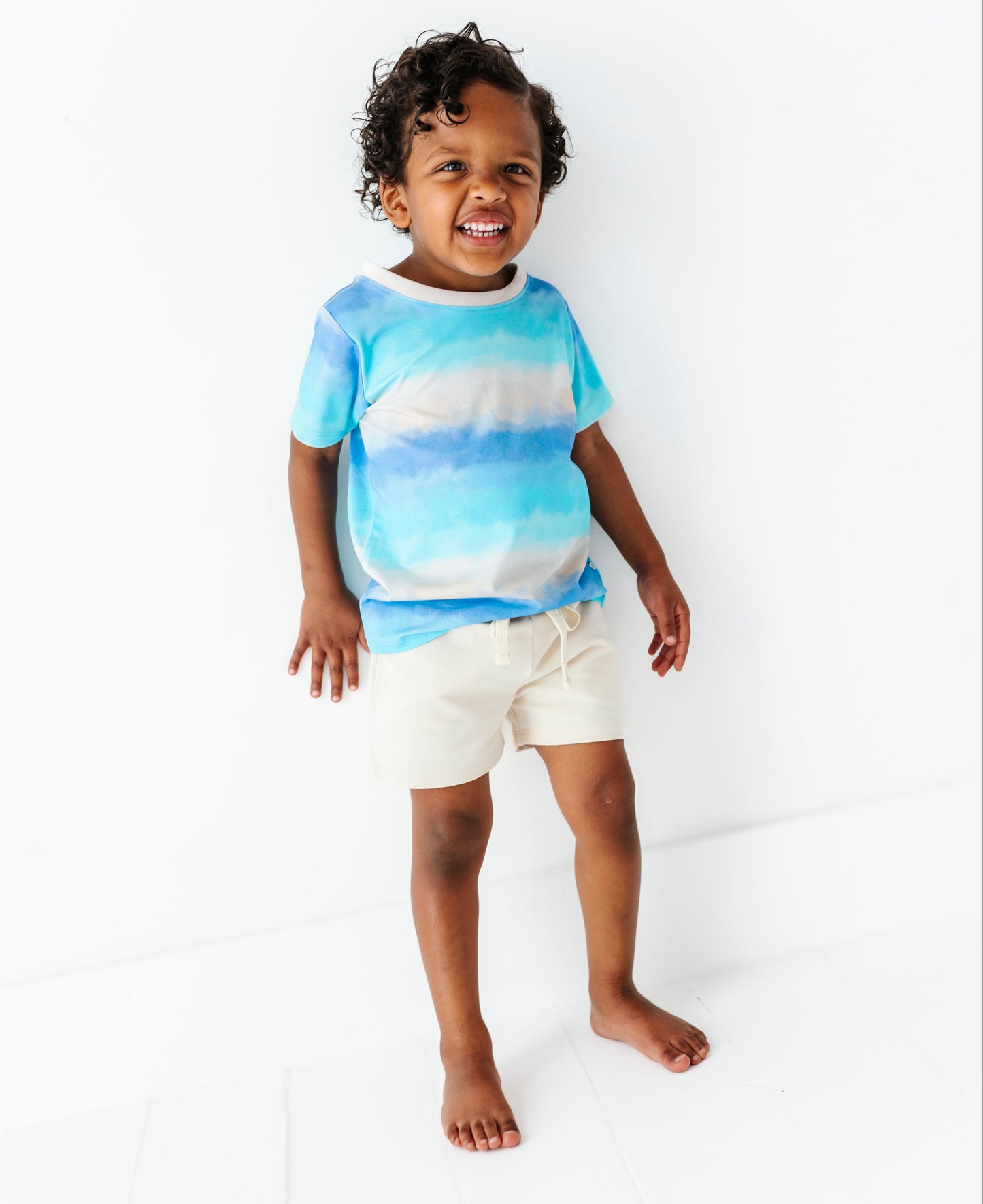 Child wearing a blue tie-dye shirt and ivory bamboo-cotton shorts on a white background