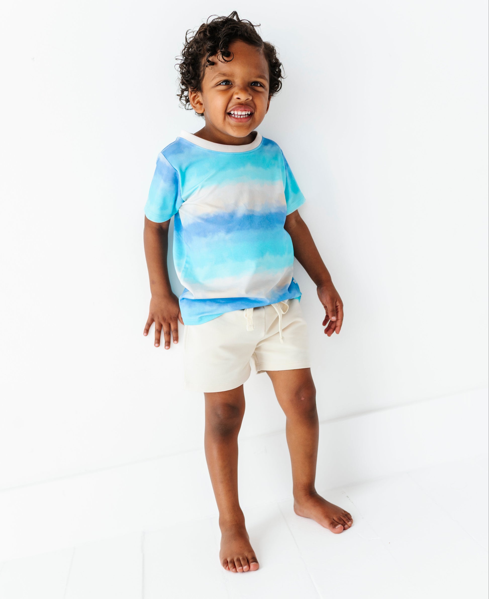Child wearing a blue tie-dye shirt and ivory bamboo-cotton shorts on a white background