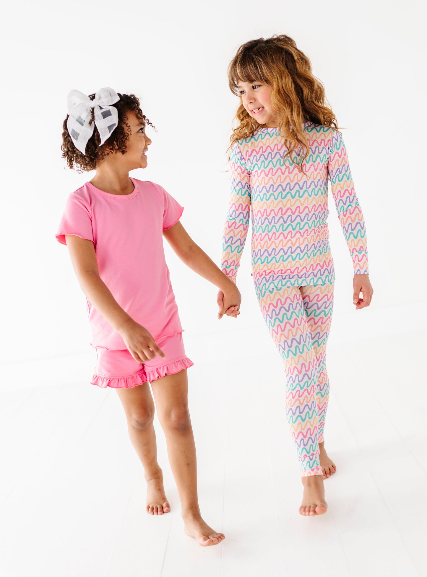 Two little girls walking together, one wearing bamboo pajamas and a pink bamboo/cotton top and shorts 