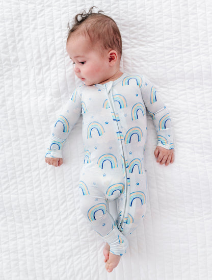 Baby wearing a bamboo convertible romper with watercolor rainbow patterns on a white textured surface