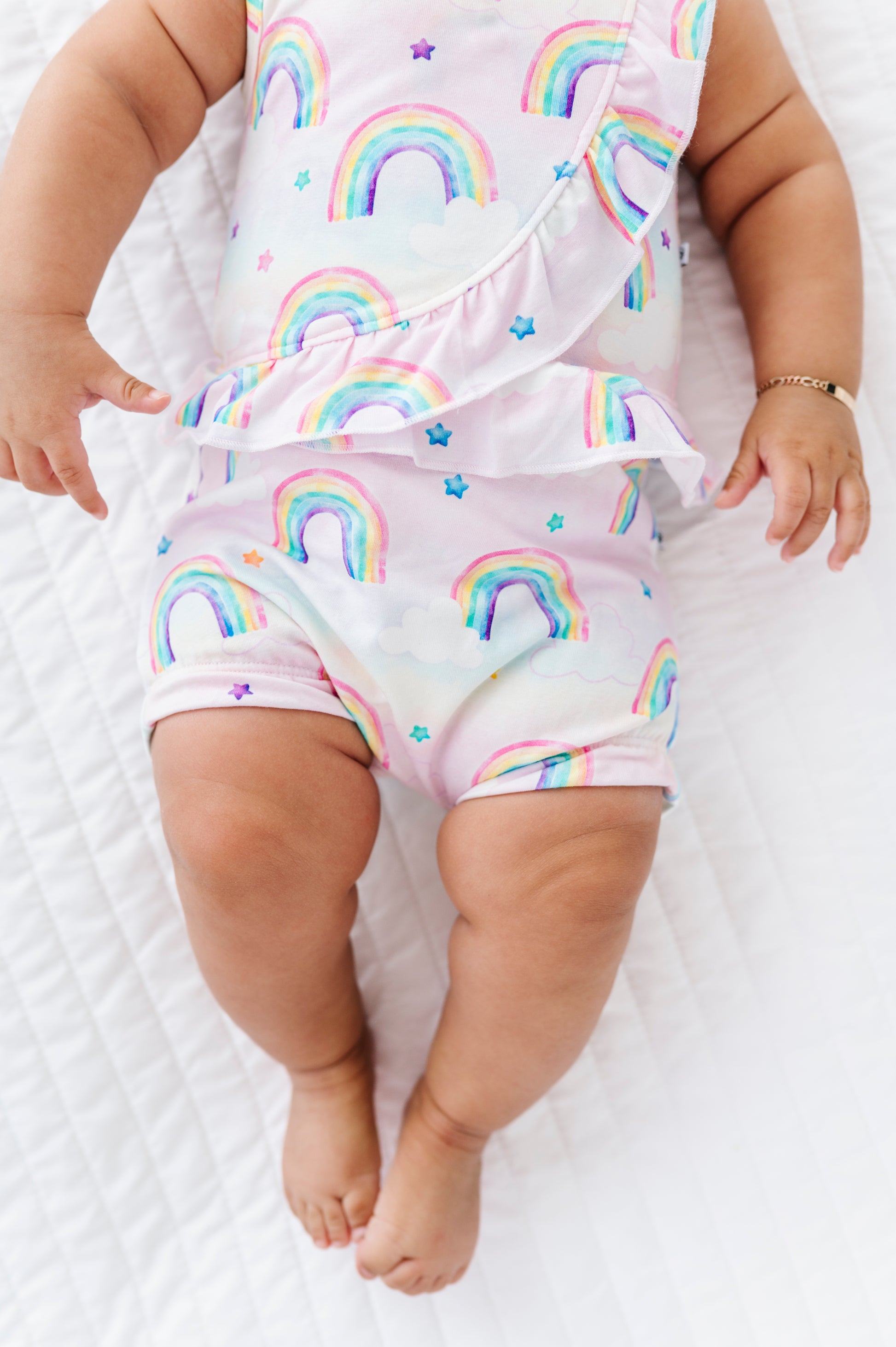 Baby wearing a bamboo cotton outfit with watercolor rainbow patterns on a white background