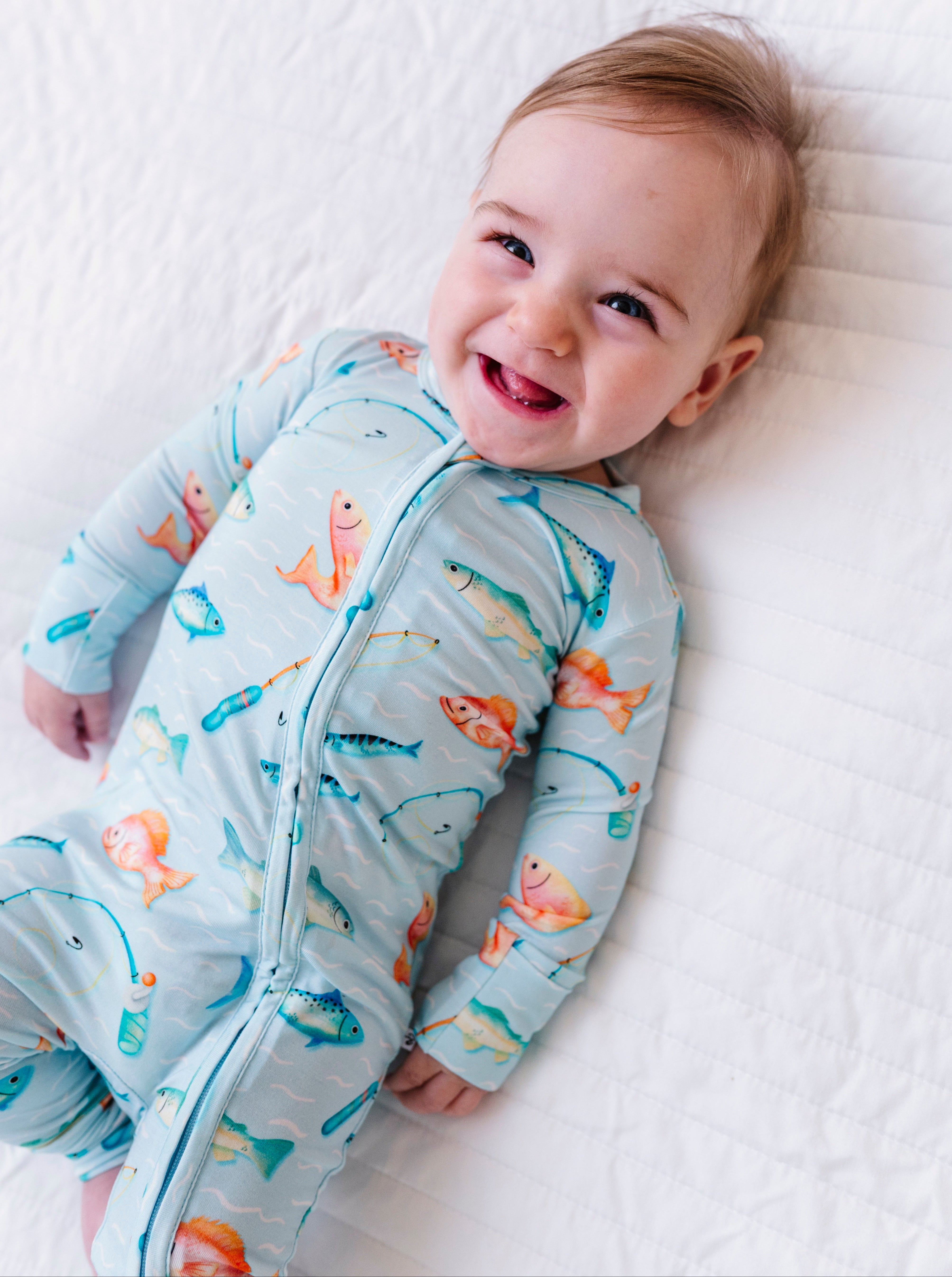 Baby wearing a fish-patterned onesie lying on a white blanket