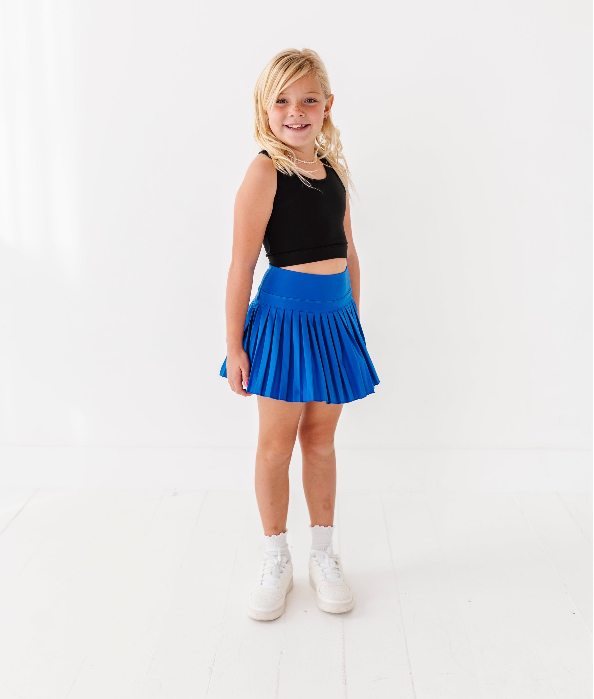 Young girl wearing a black top and blue skort on a white background