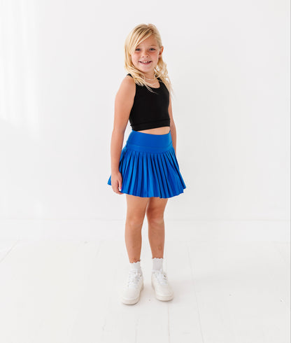 Young girl wearing a black top and blue skort on a white background