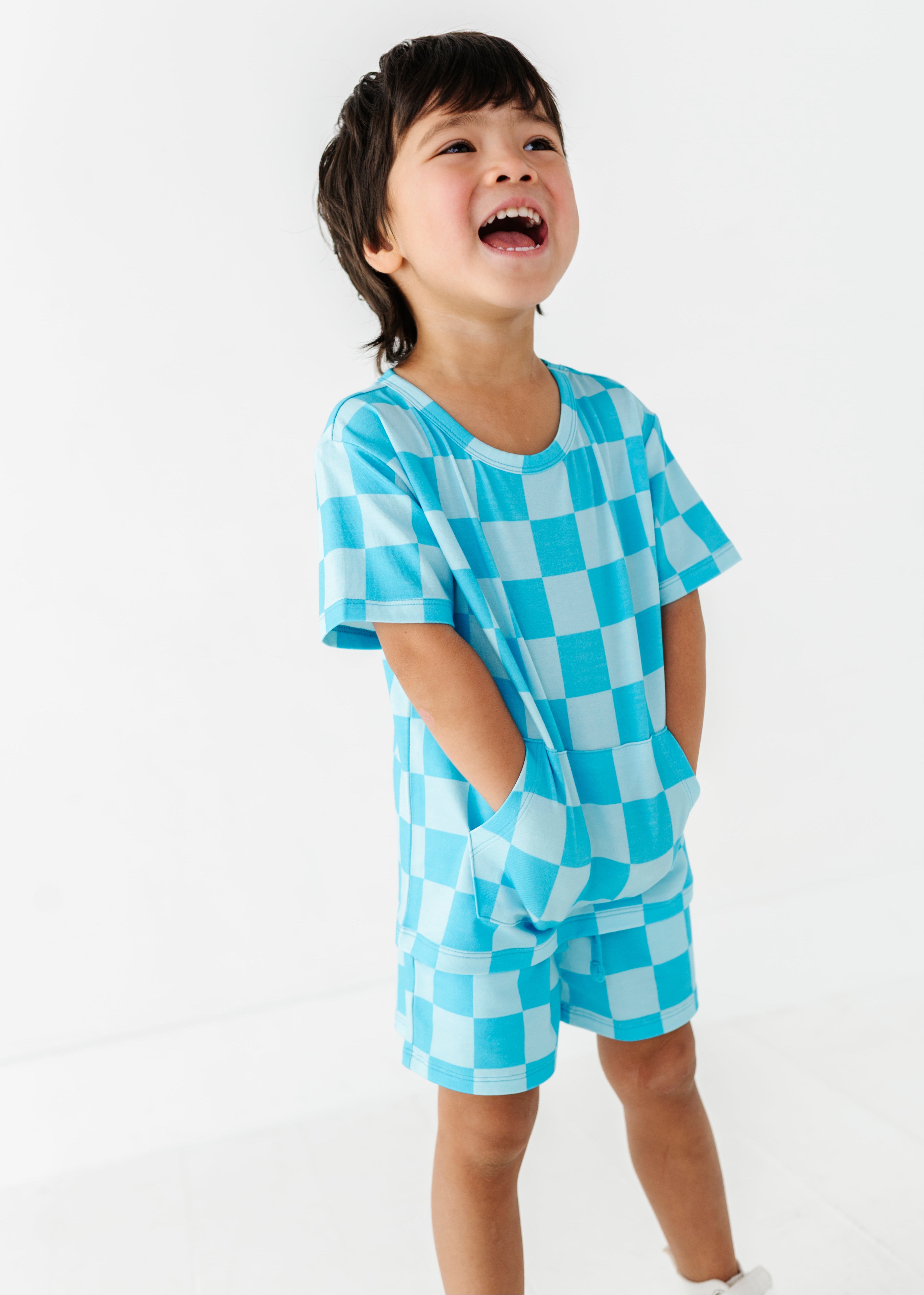 A young child wearing a light blue and white checkered short-sleeve t-shirt and matching shorts, standing against a plain white background.