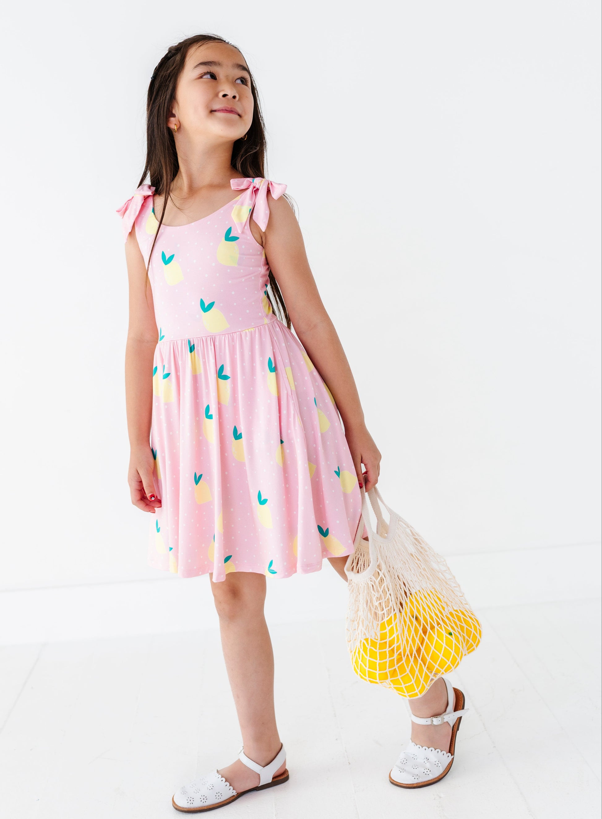 Young girl wearing a pink dress with colorful patterns, holding a yellow bag, on a white background