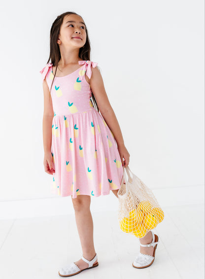 Young girl wearing a pink dress with colorful patterns, holding a yellow bag, on a white background