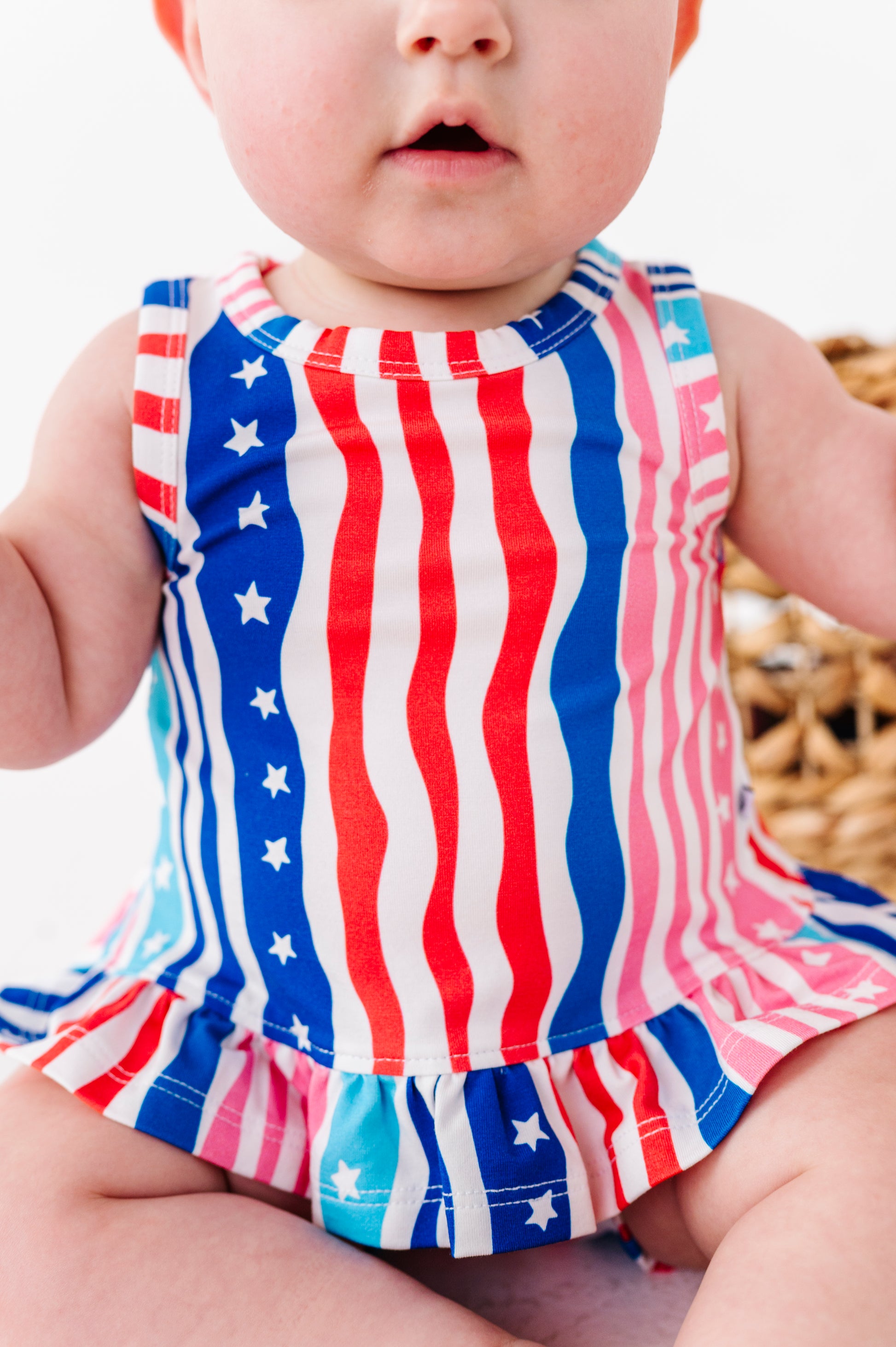 Baby wearing a red, white, and blue striped swing top with star patterns.