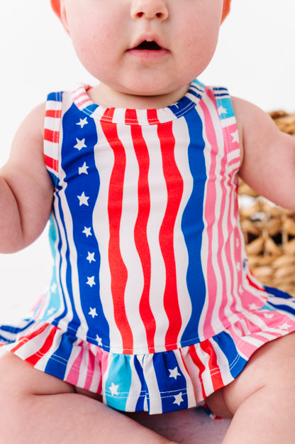 Baby wearing a red, white, and blue striped swing top with star patterns.