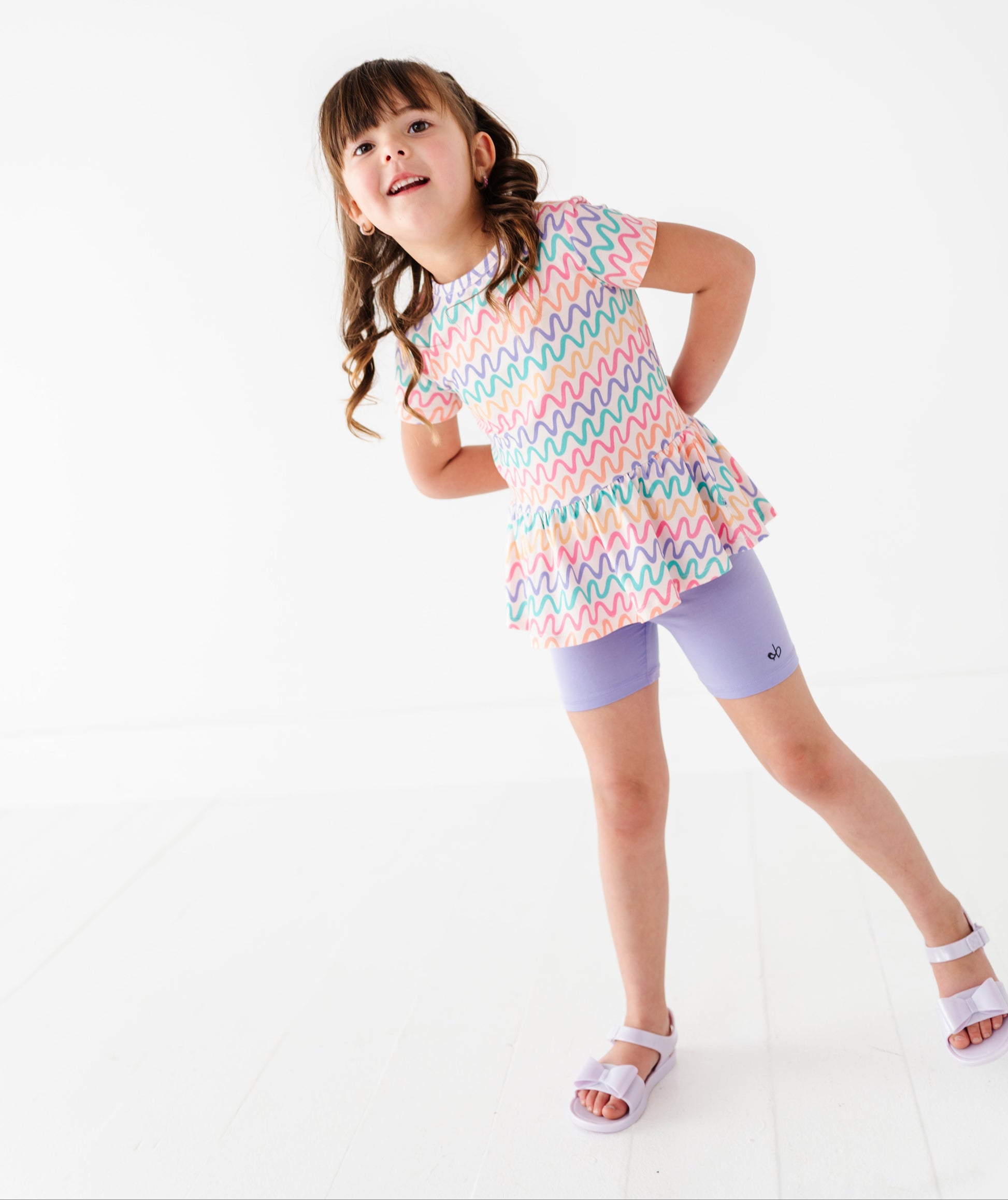 Young girl wearing a colorful bamboo/cotton top and light purple biker shorts on a white background