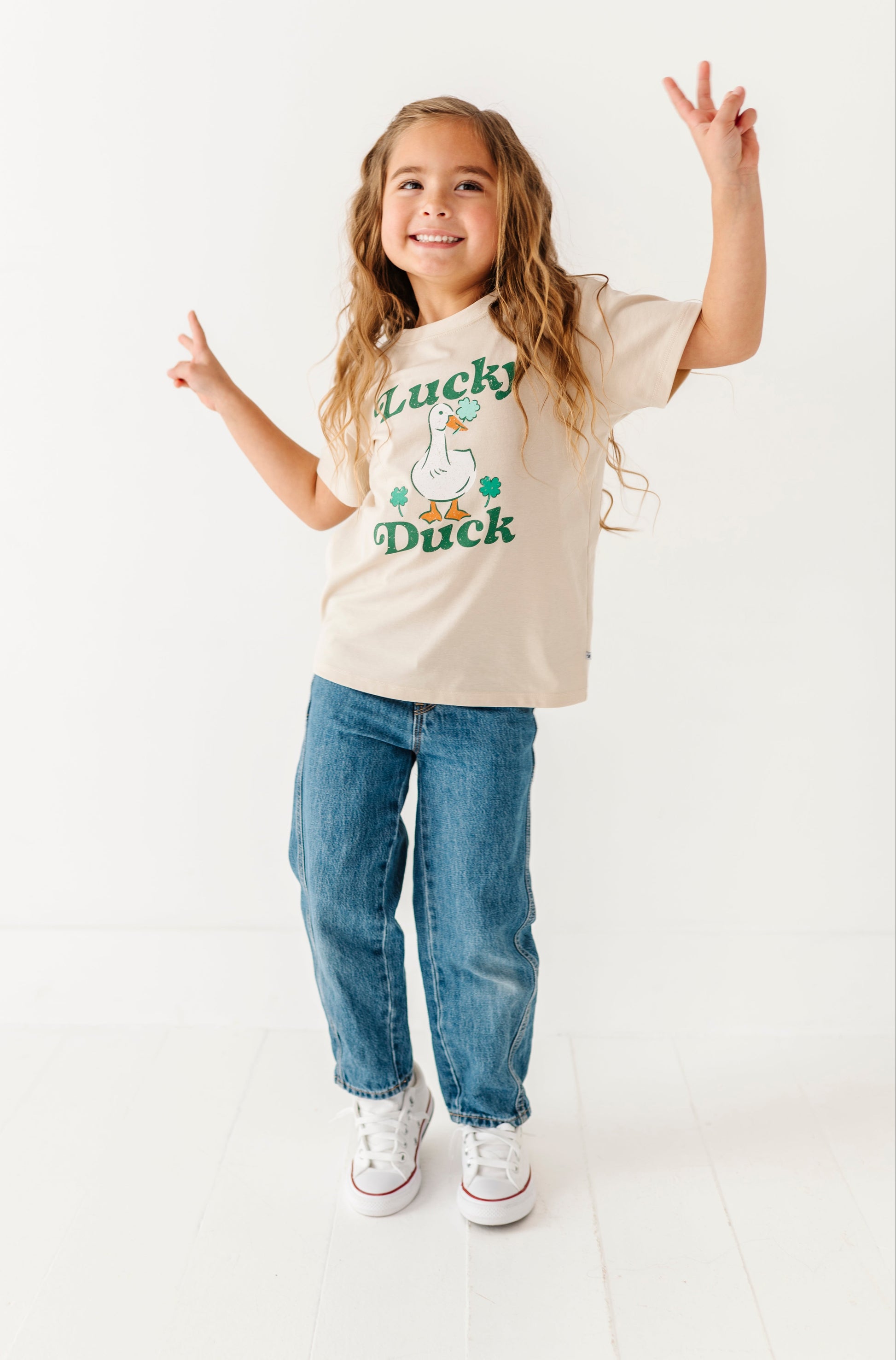 Child wearing a 'Lucky Duck' t-shirt and blue jeans on a white background
