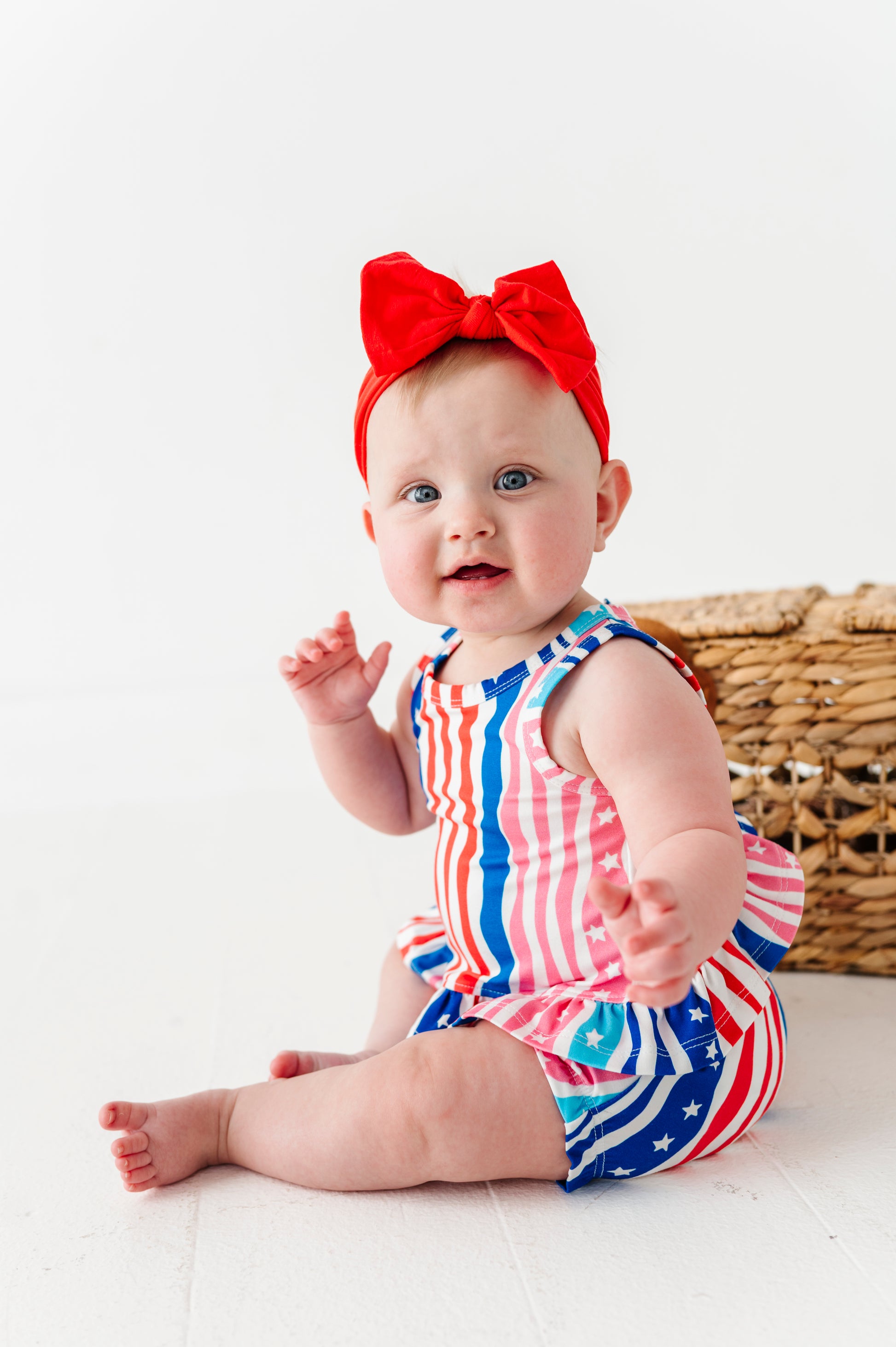 Baby wearing a red, white, and blue striped bamboo swing top set with a large red bow on a white background