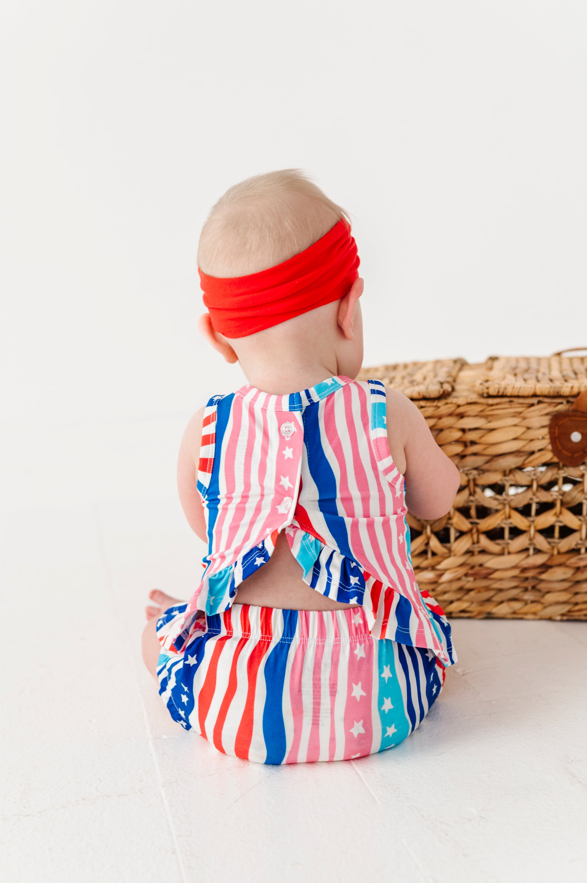 Baby wearing a red, white, and blue bamboo-cotton swing top set with a headband on a white background