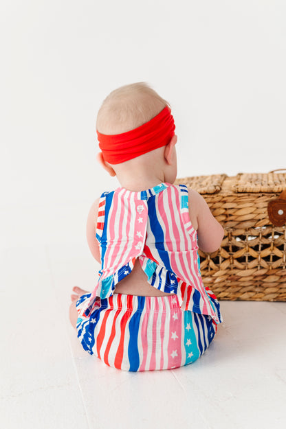 Baby wearing a red, white, and blue bamboo-cotton swing top set with a headband on a white background