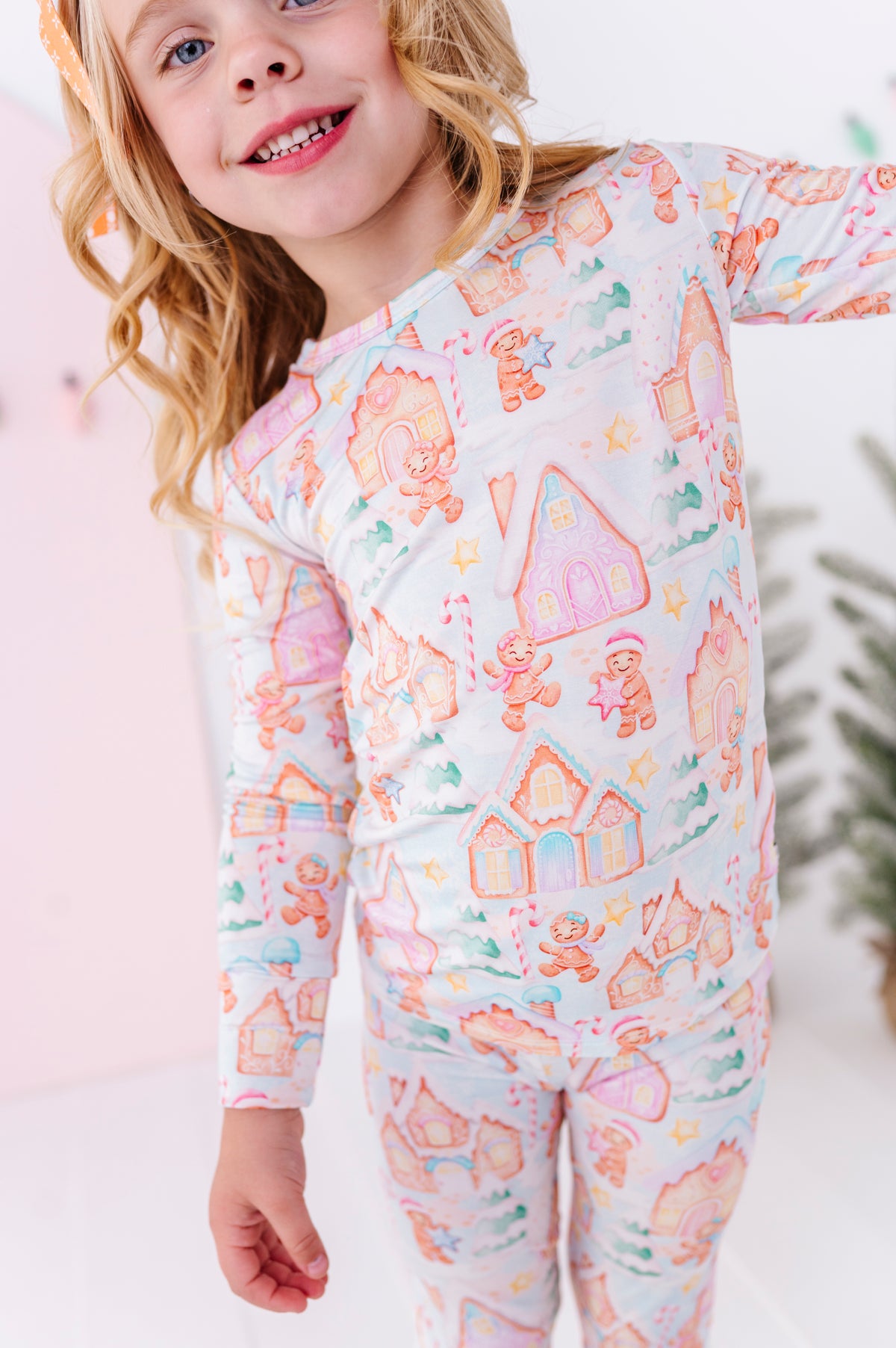 A young girl wearing a long-sleeve two-piece bamboo pajama with a colorful gingerbread house and candy cane pattern on a white background.