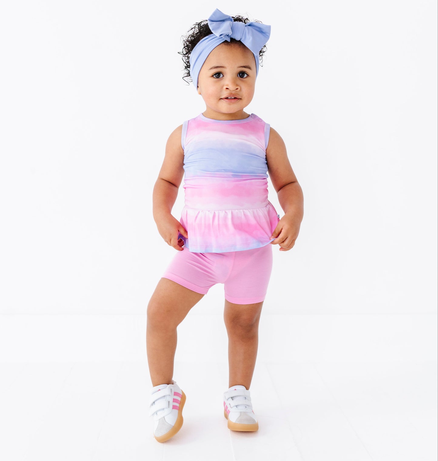 Baby wearing a colorful tie-dye bamboo-cotton peplum top with pink shorts on a white background