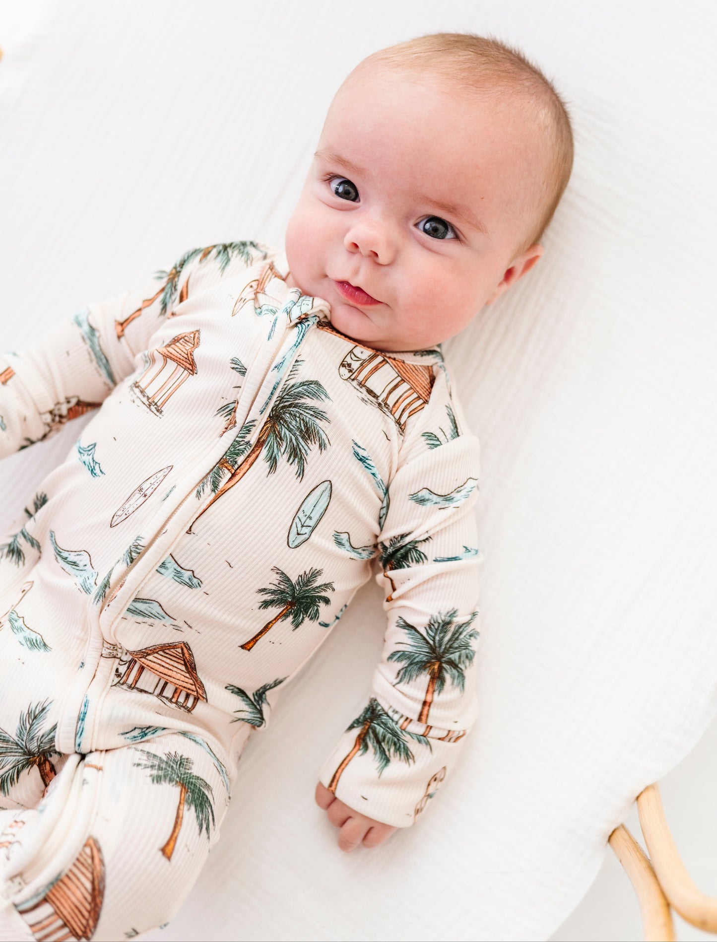 Baby wearing a romper with palm tree design on a white background