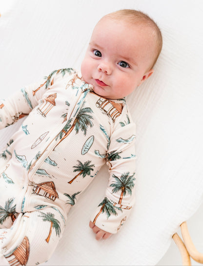 Baby wearing a romper with palm tree design on a white background