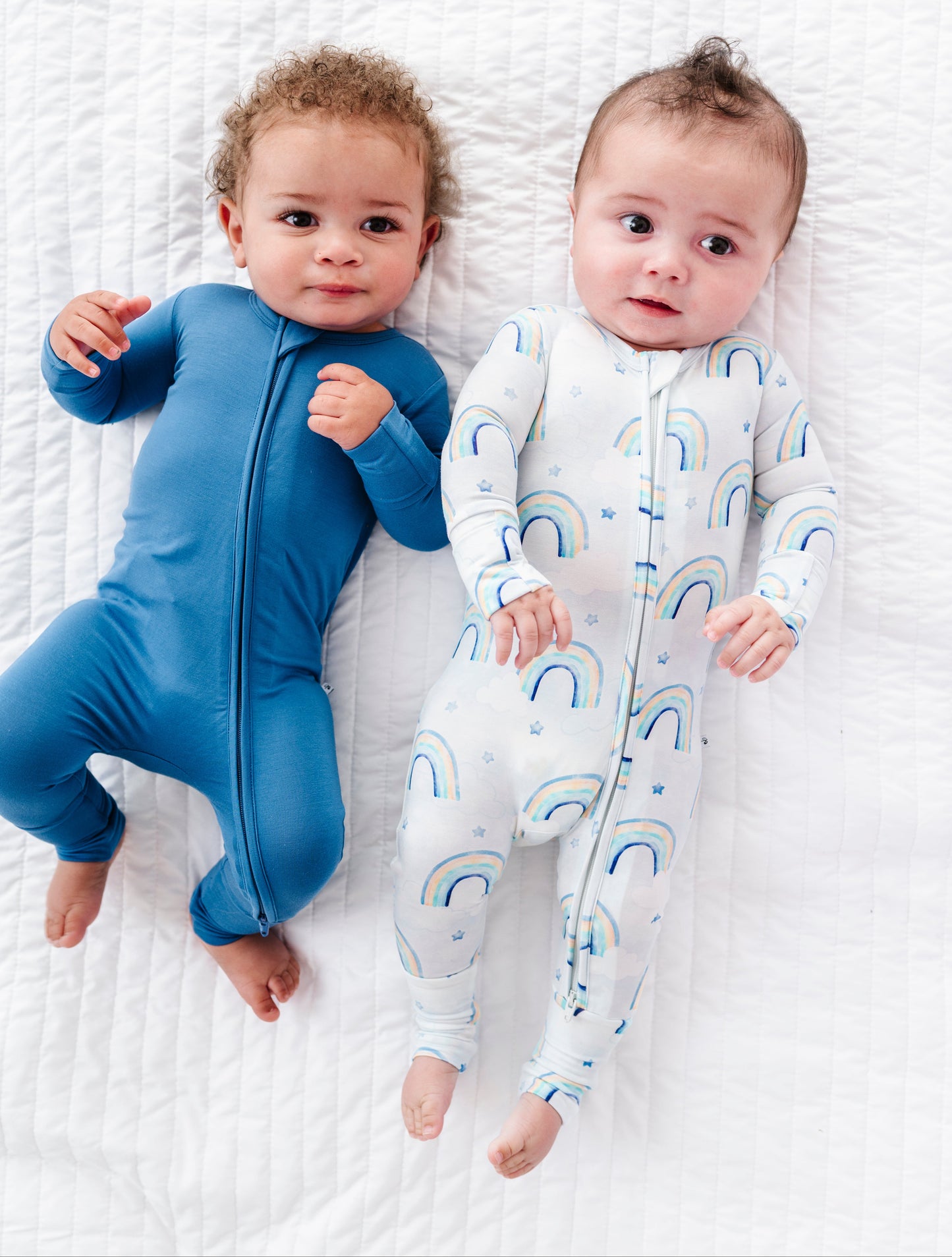 Two babies wearing bamboo zip rompers on a white textured surface