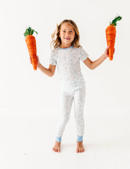 Child wearing a blue and white patterned Easter pajamas holding two large toy carrots.