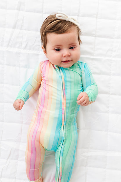 Baby wearing a rainbow stripe bamboo convertible romper with mint, pink, and pastel stripes on a white quilted background