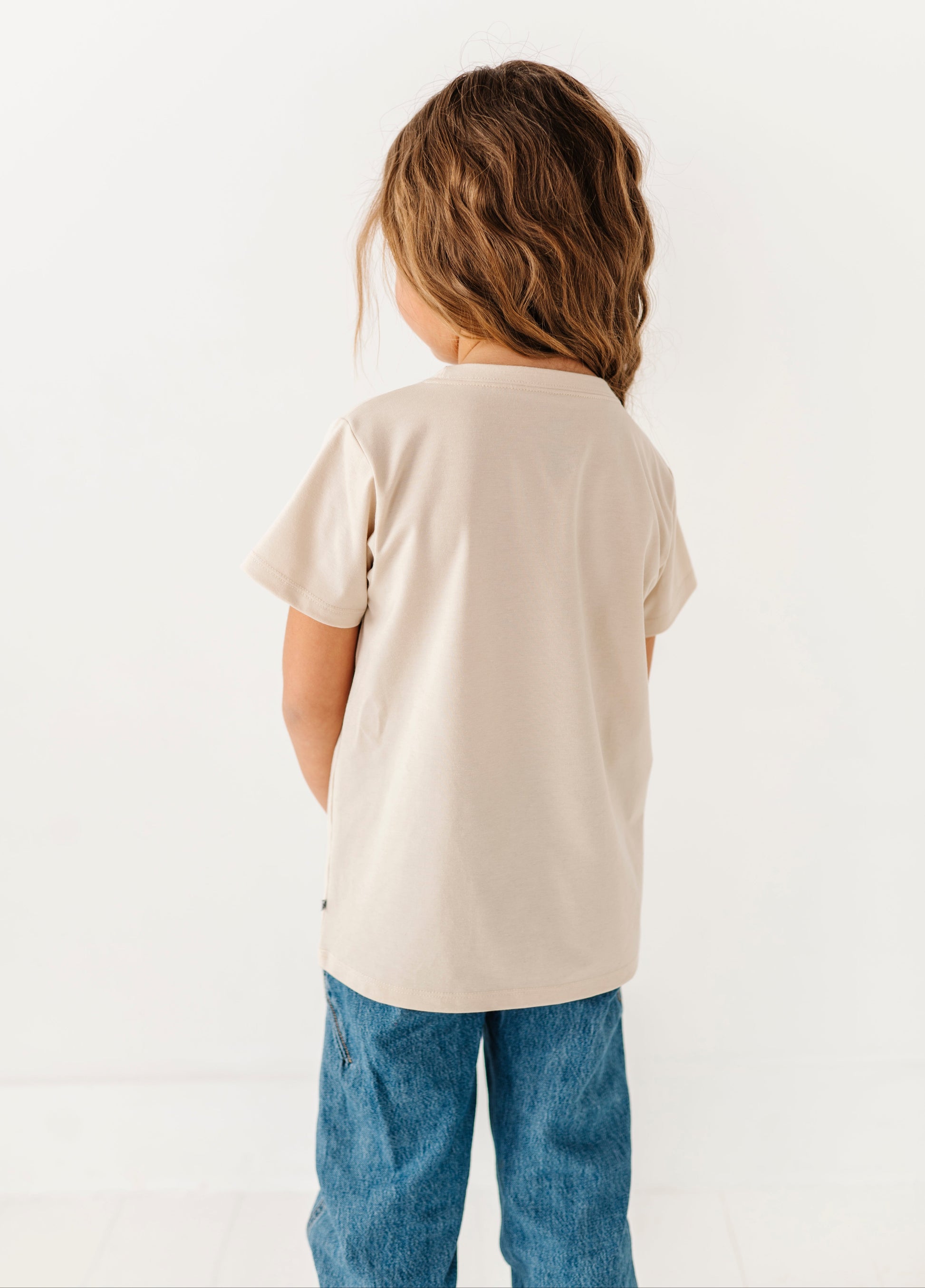 Child wearing a beige t-shirt and blue jeans on a white background