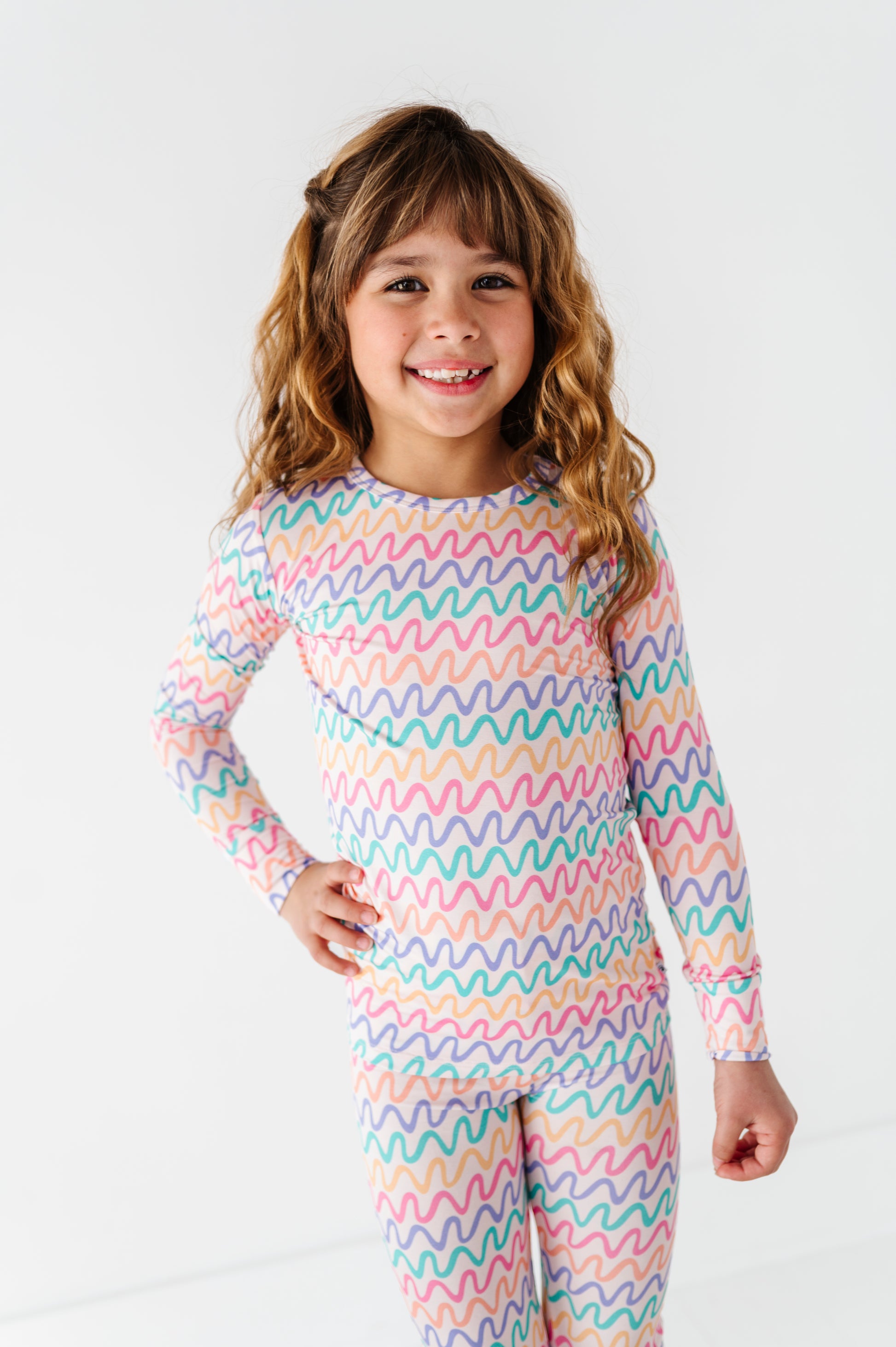 Young girl wearing a colorful wavy patterned bamboo two-piece pajama set on a white background
