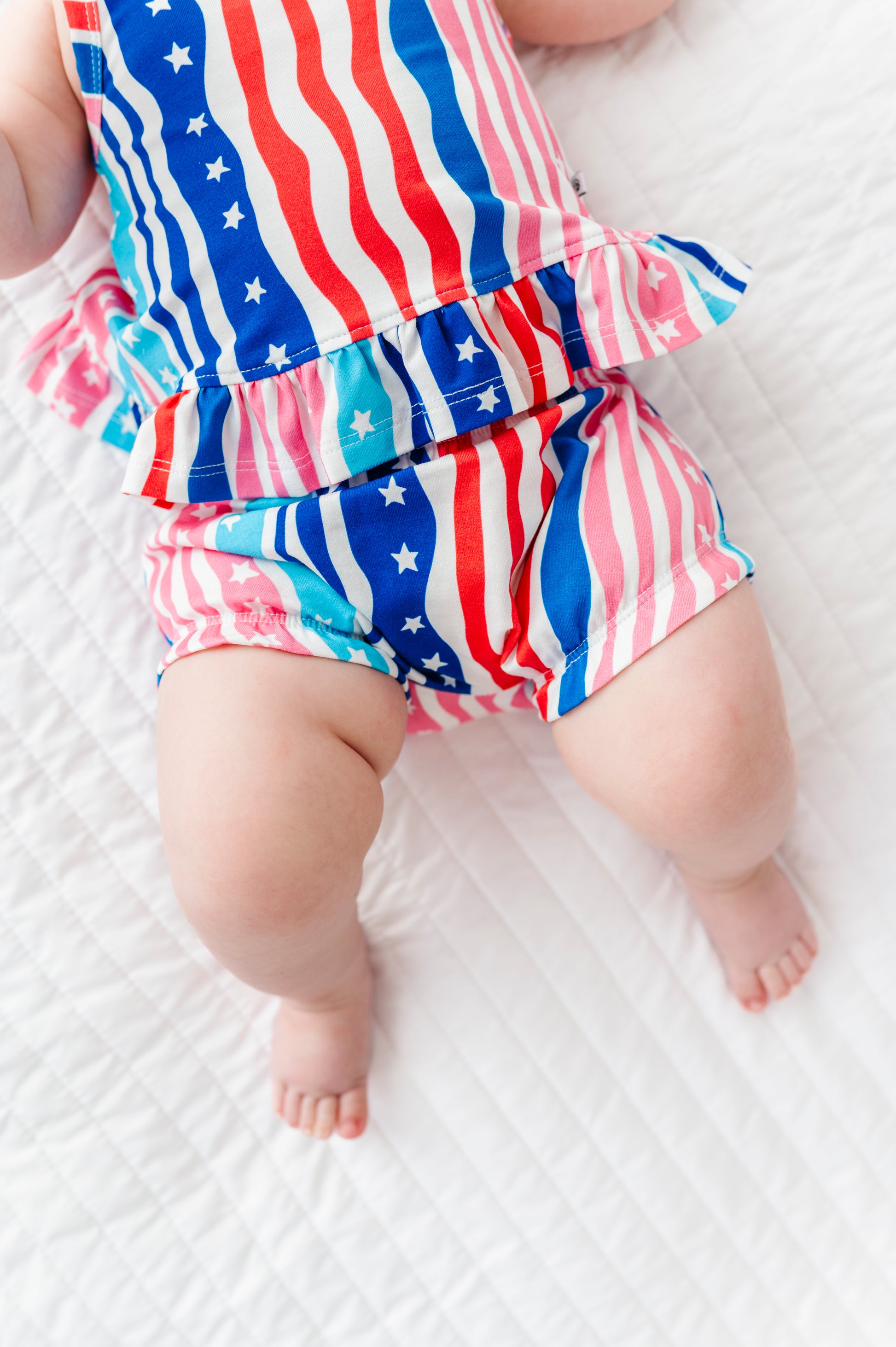 Baby wearing a red, white, and blue striped Fourth of July outfit on a white background
