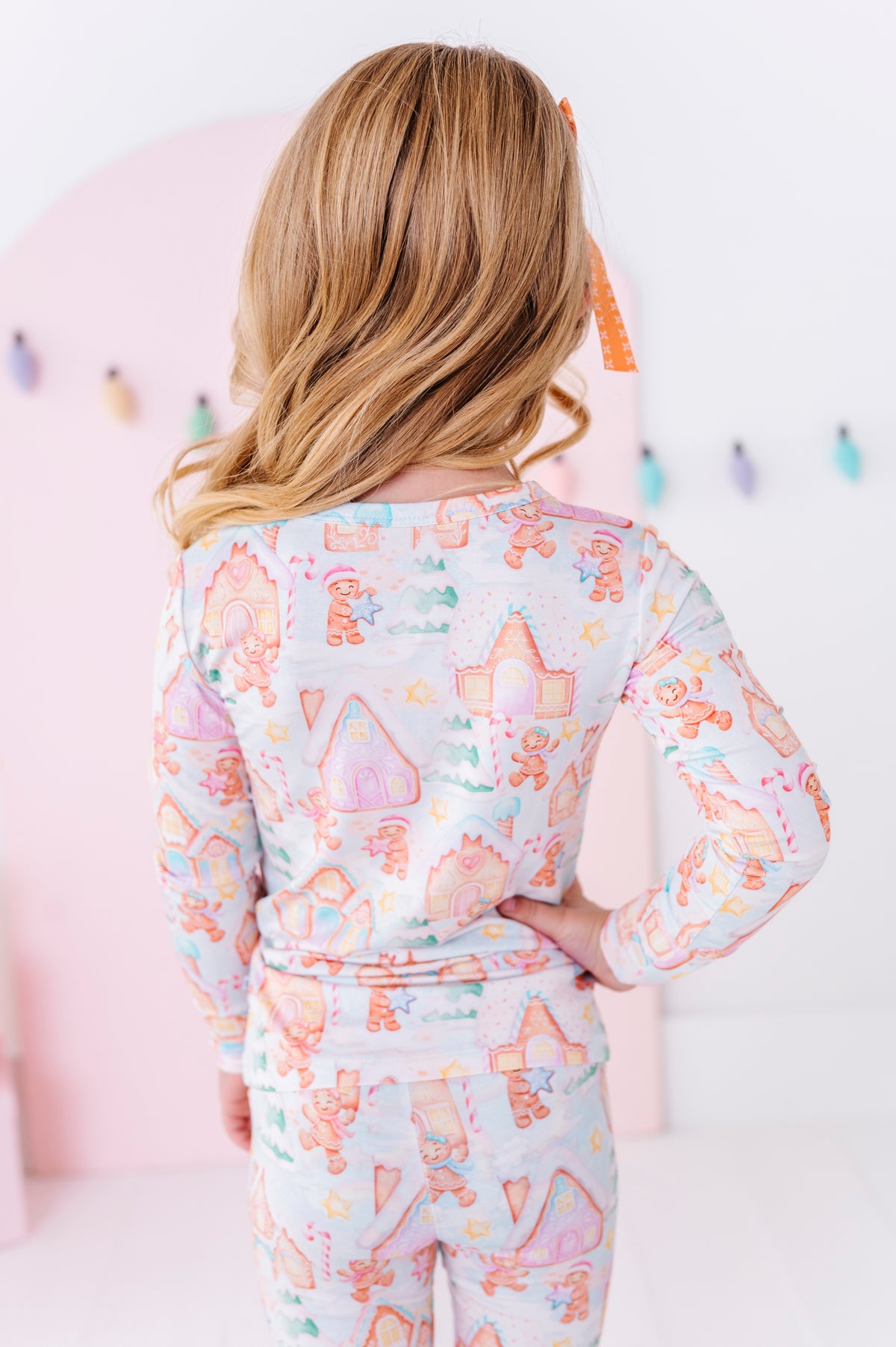 A child viewed from behind wearing a long-sleeve bamboo pajama top and matching pants with a whimsical pastel print of houses, trees, and stars on a light background.