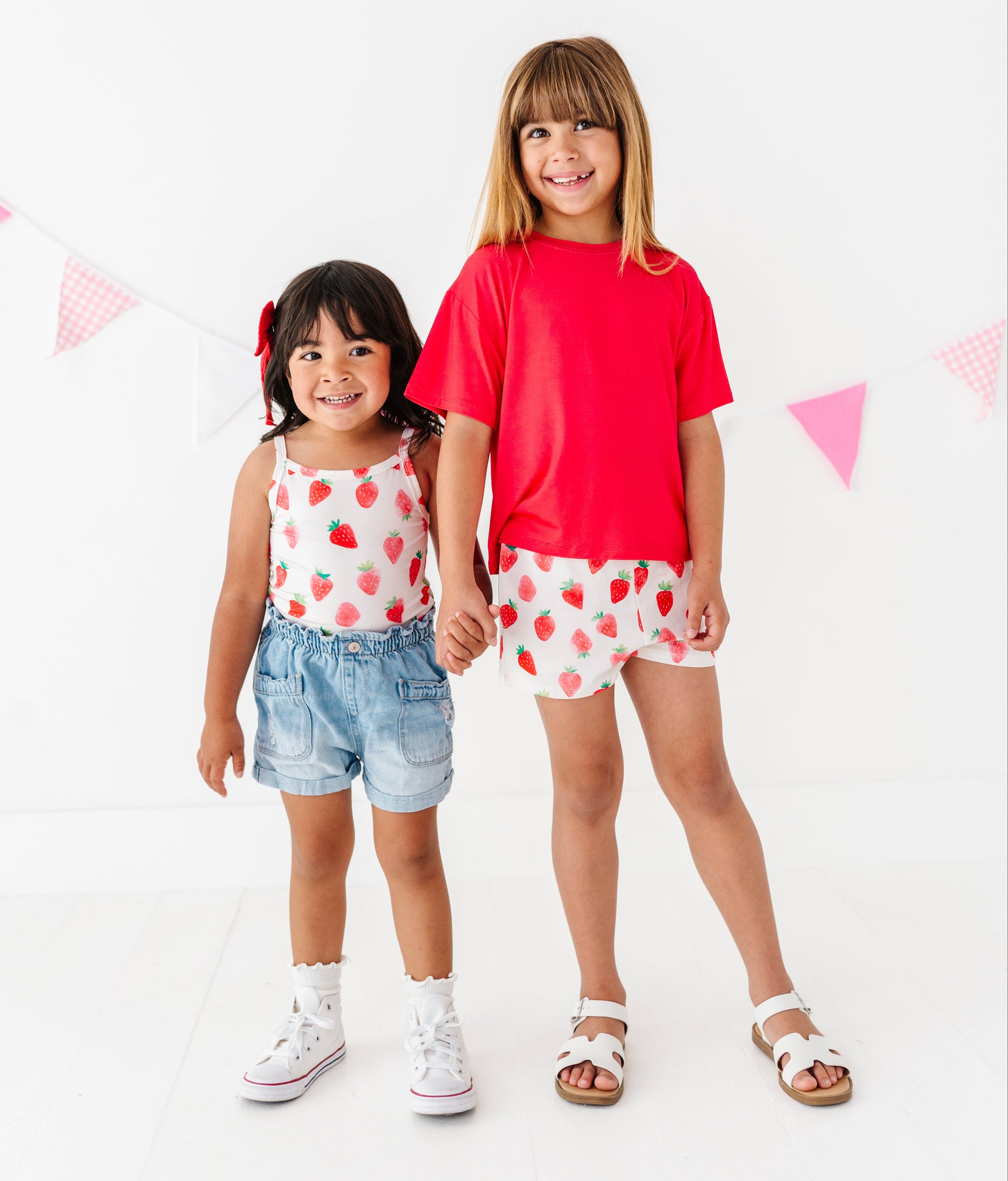 Two young girls wearing matching outfits standing against a white background with pink triangle flags.