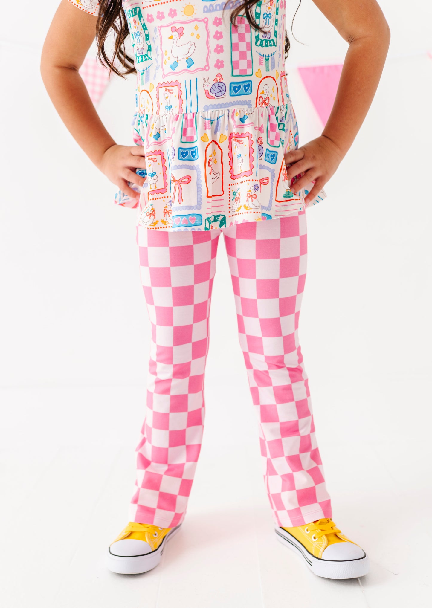 Child wearing a colorful outfit with pink checkered pants and yellow shoes on a white background