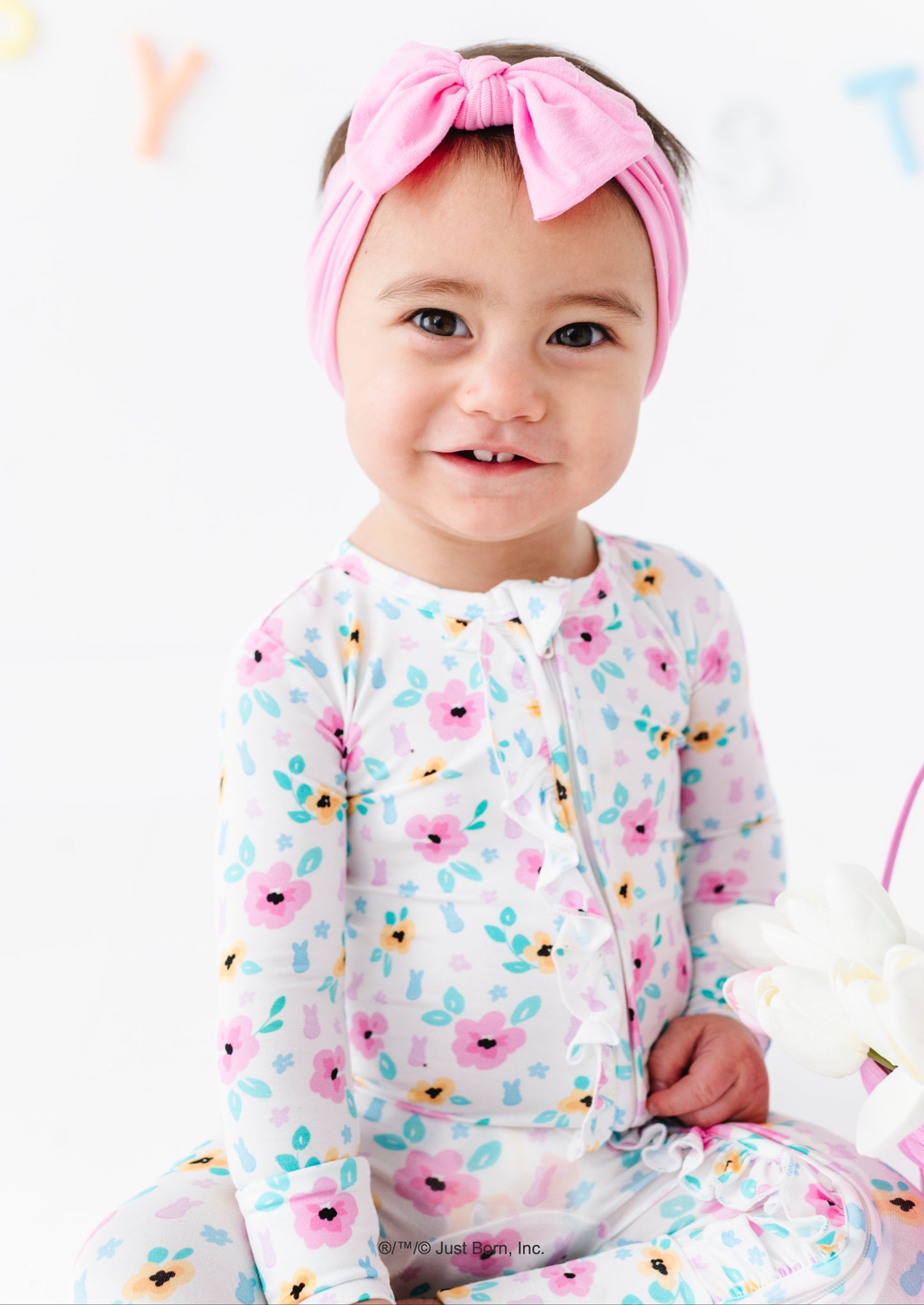 Baby wearing a floral PEEPS® romper and pink headband on a white background