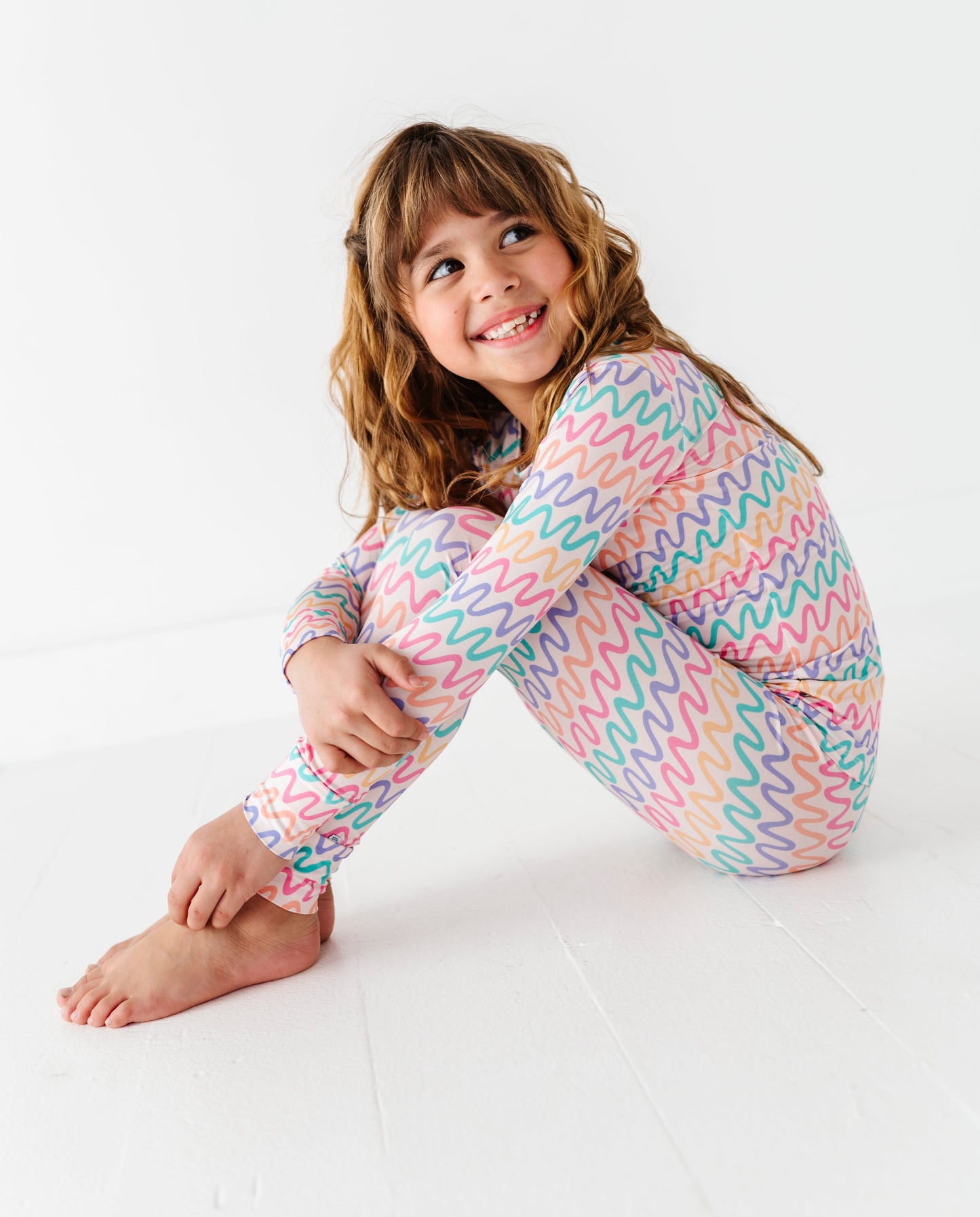 Child wearing a colorful wavy patterned bamboo two-piece pajama set on a white background