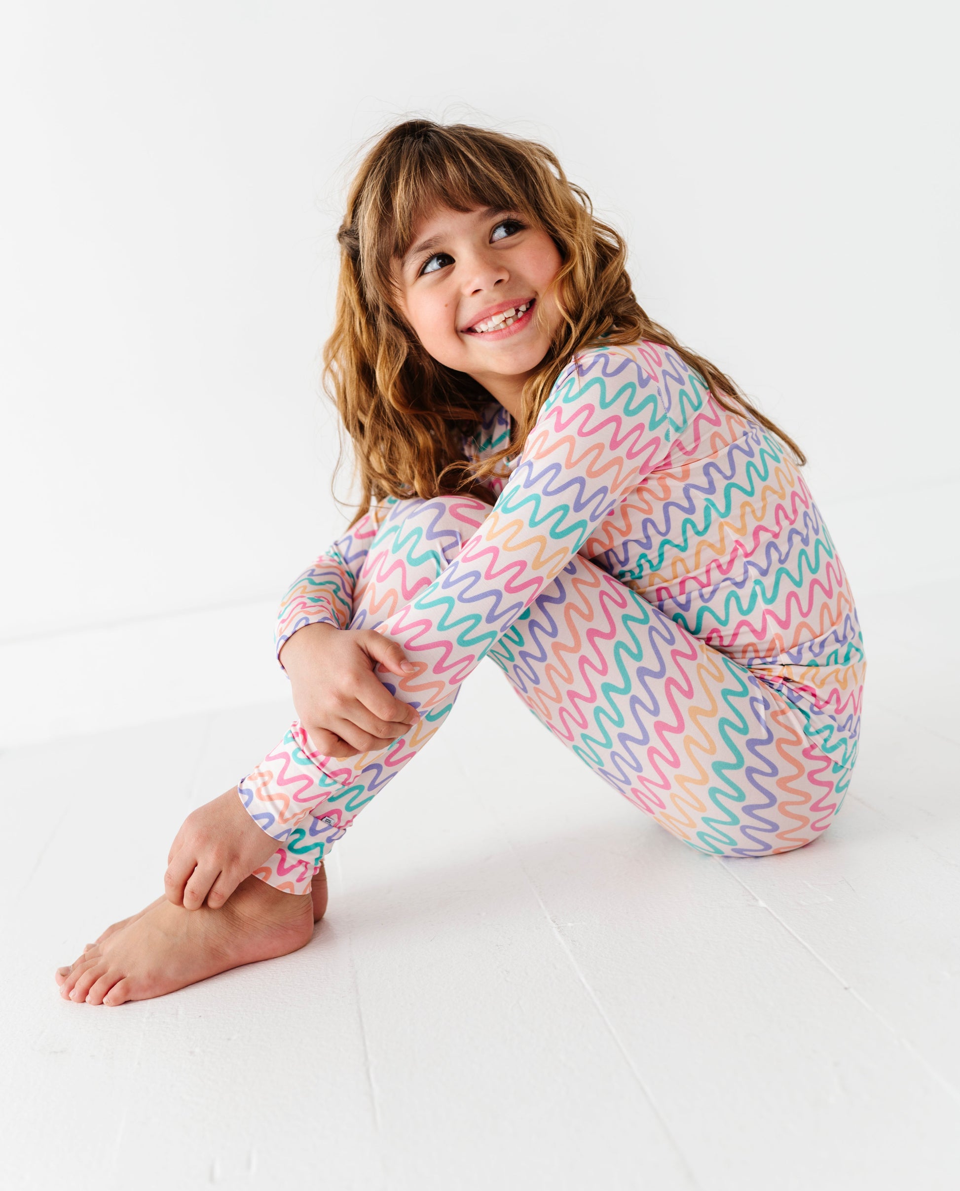 Child wearing a colorful wavy patterned bamboo two-piece pajama set on a white background