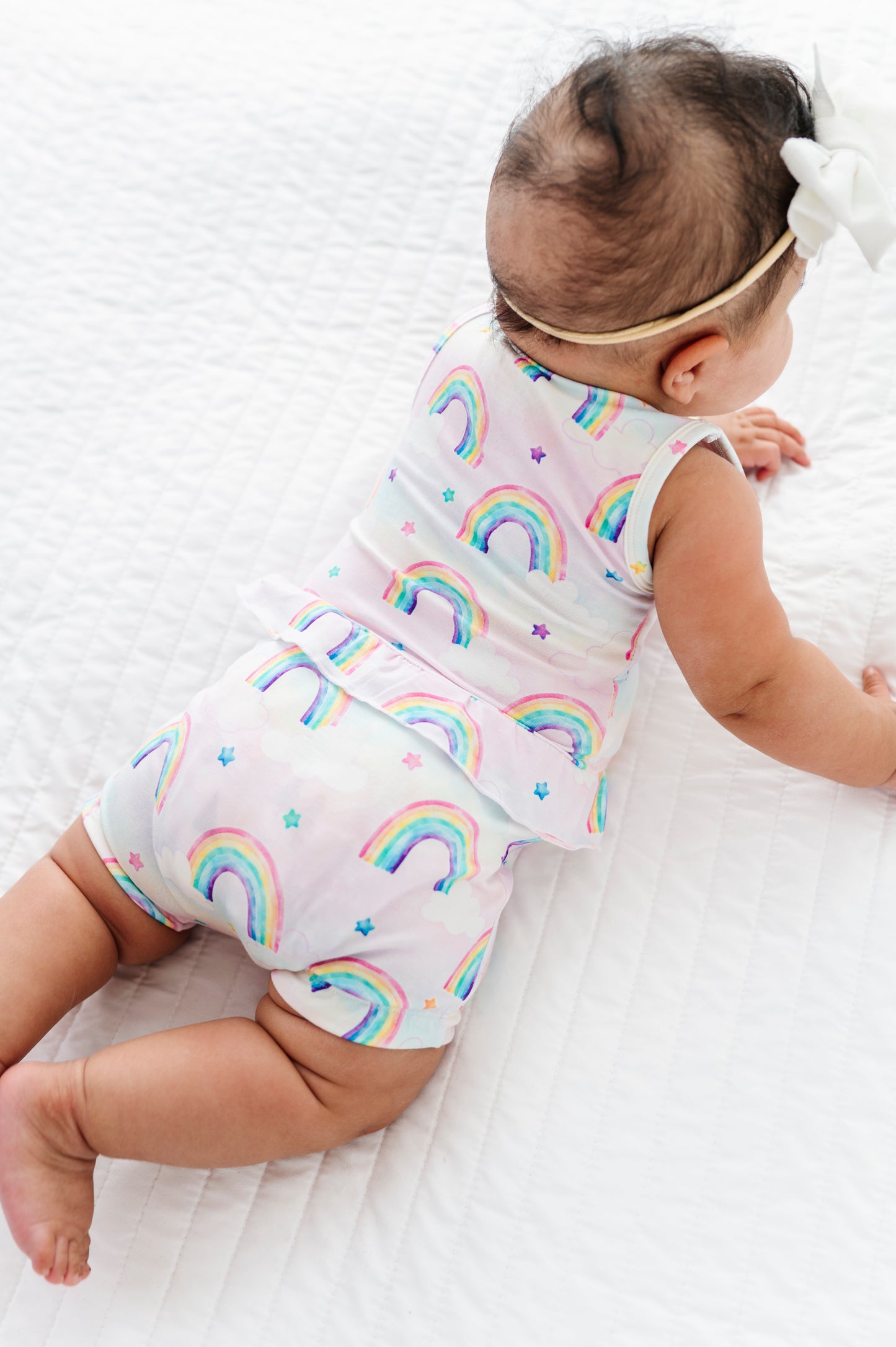 Baby wearing a rainbow-patterned bamboo peplum set on a white background