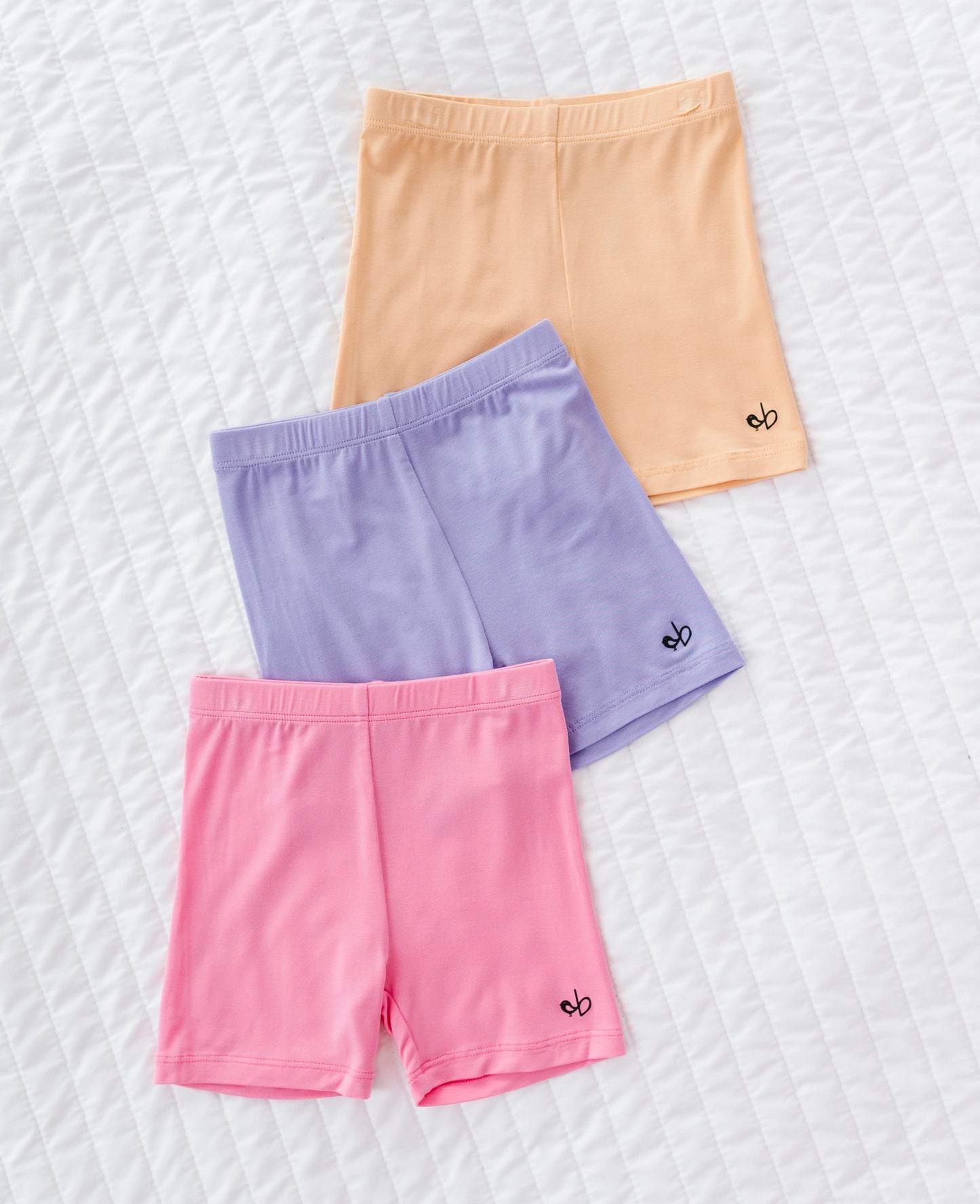 Three pairs of colorful bamboo shorts (yellow, purple, pink) on a textured white background