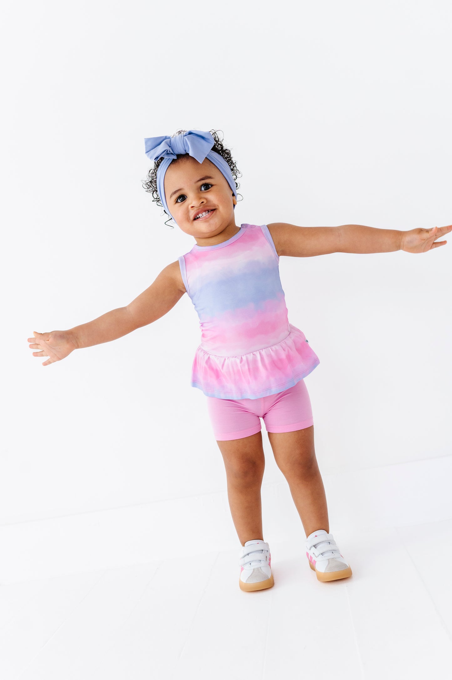 Child wearing a tie-dye bamboo-cotton peplum top paired with pink bamboo biker shorts on a white background