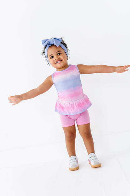 Child wearing a tie-dye bamboo-cotton peplum top paired with pink bamboo biker shorts on a white background