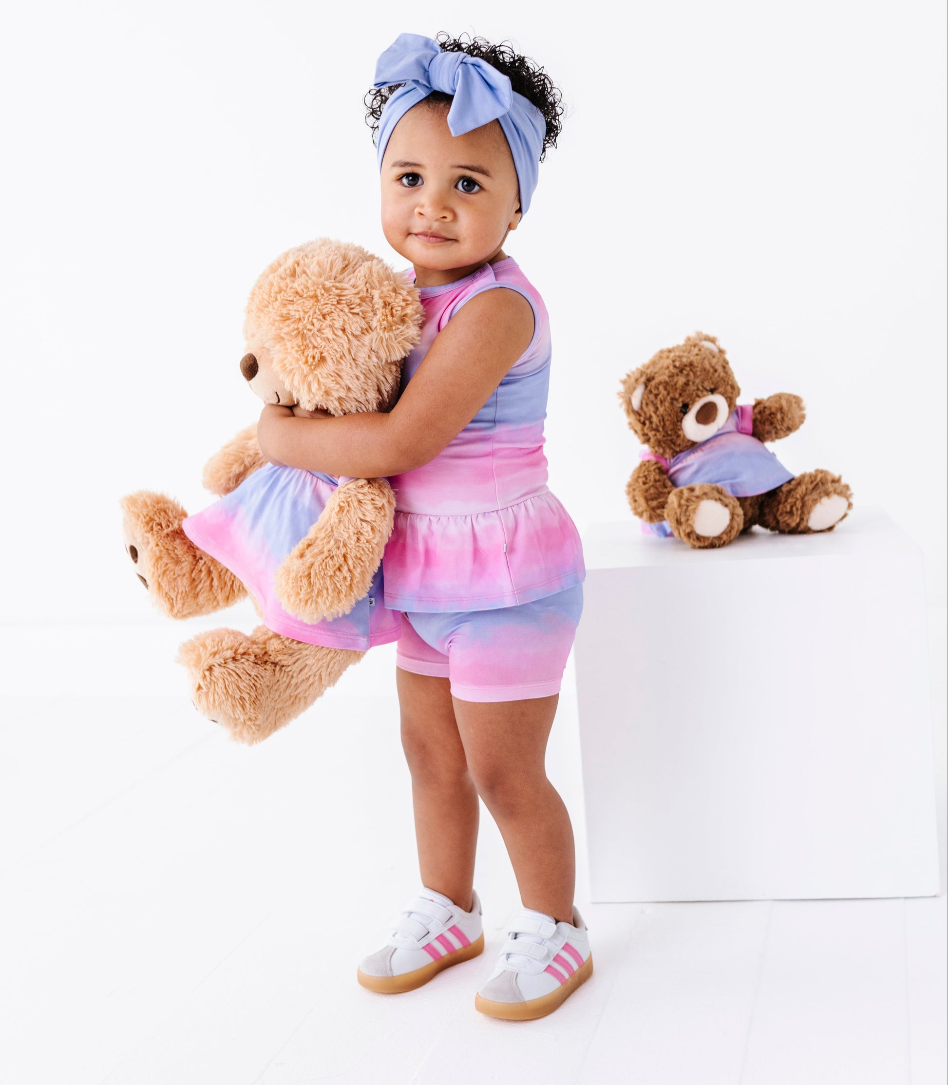 Child wearing a colorful bamboo-cotton peplum top holding a teddy bear with another teddy bear in the background.