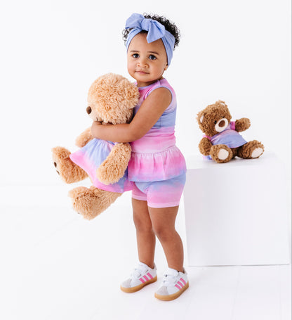 Little girl and her teddy bear wearing matching pink and purple ombre dresses 